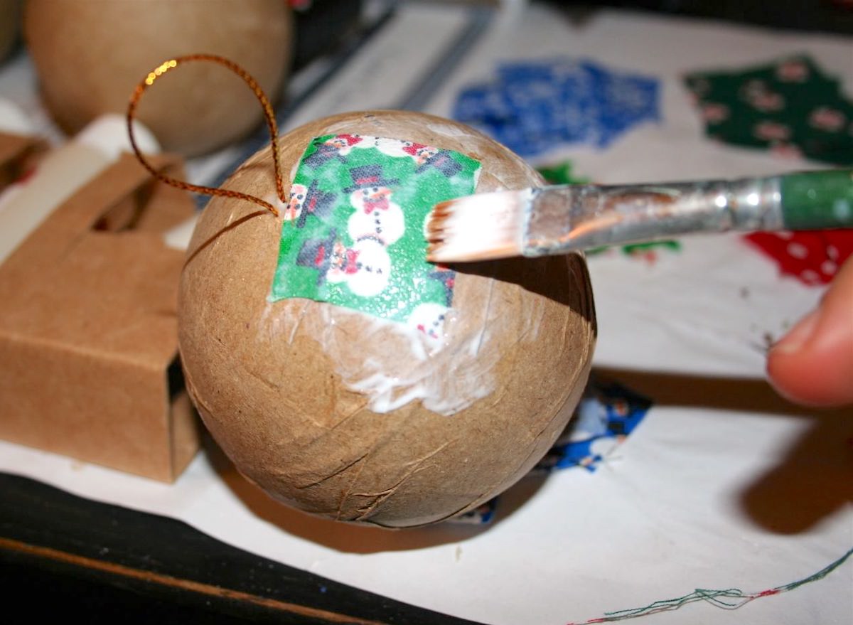 Applying a square of fabric to a paper mache ornament with a paintbrush and Mod Podge