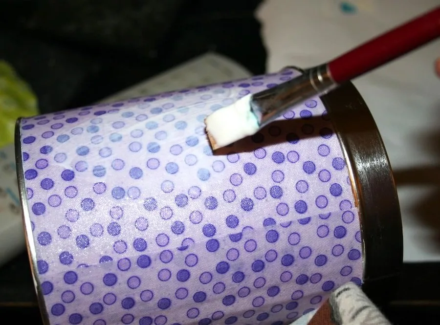 Placing Mod Podge over the top of purple fabric on a tin