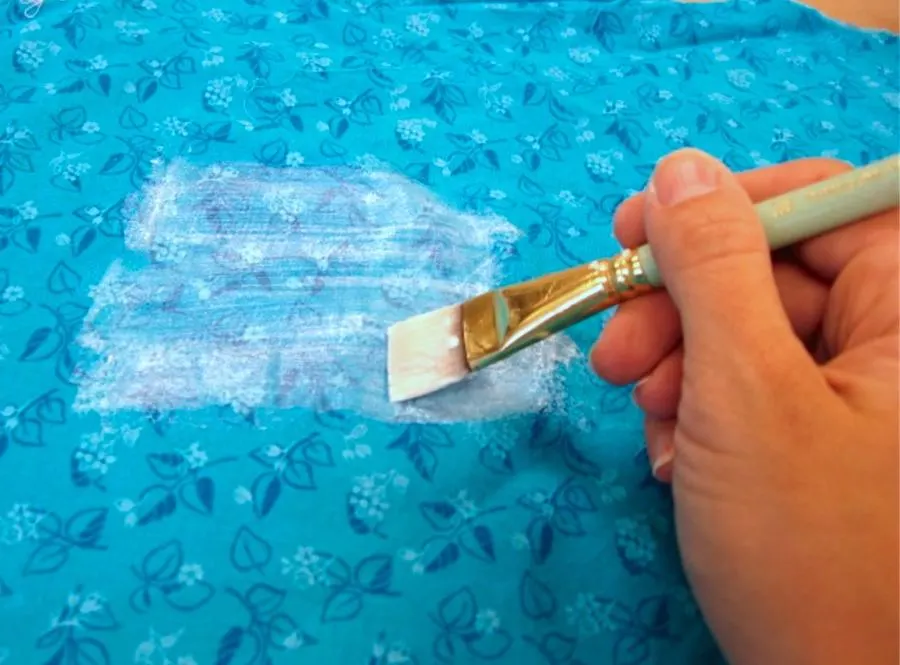Spreading Mod podge over blue fabric on a work surface