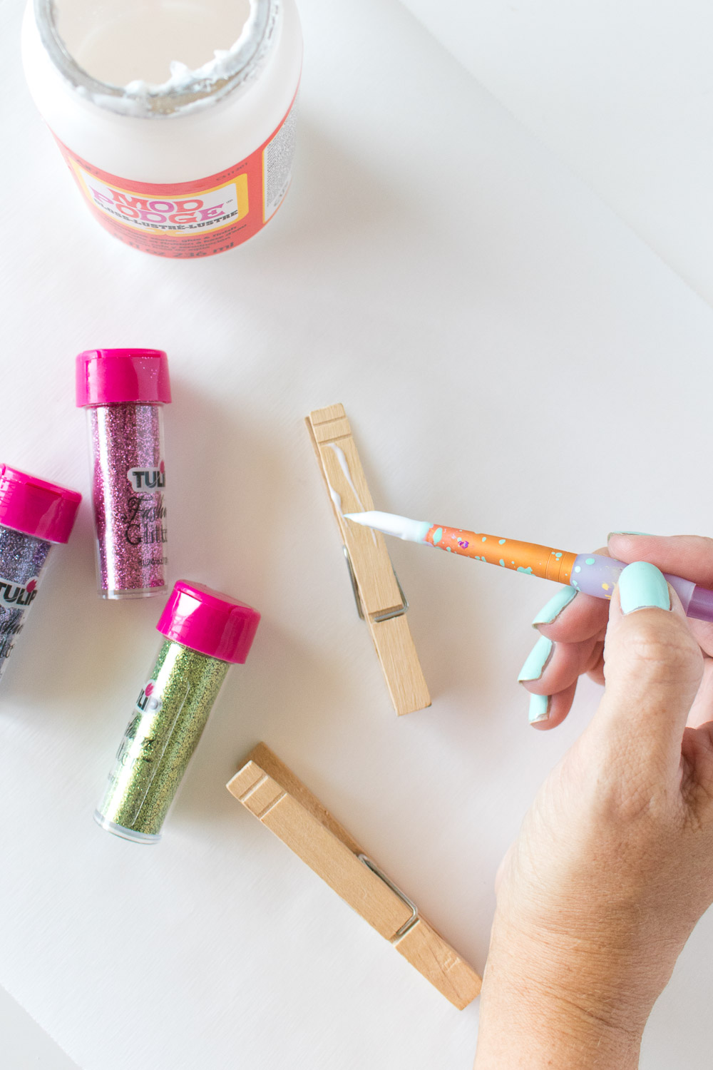 painting mod podge on the top of a clothespin with a paintbrush