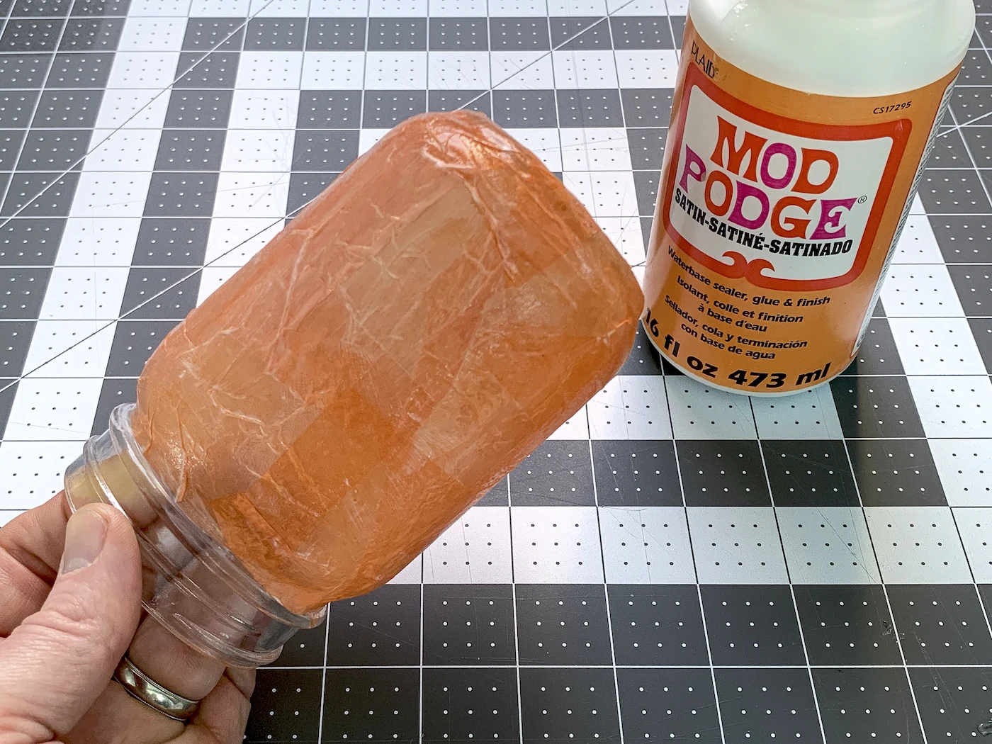 Mason jar covered in orange tissue paper with a bottle of Mod Podge sitting next to it