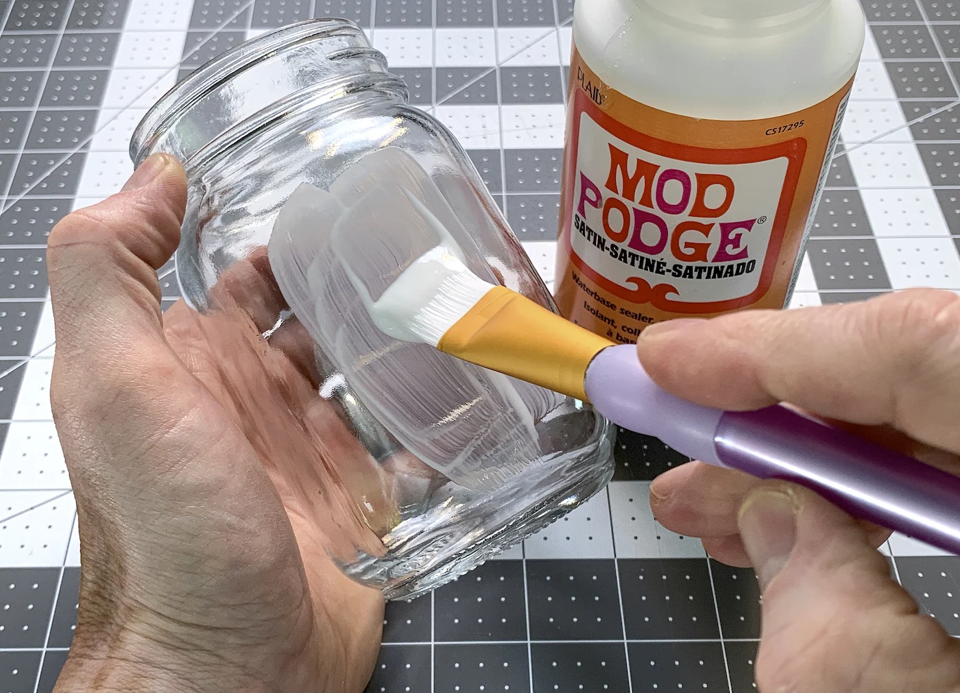 Painting Mod Podge on the outside of a mason jar with a paintbrush
