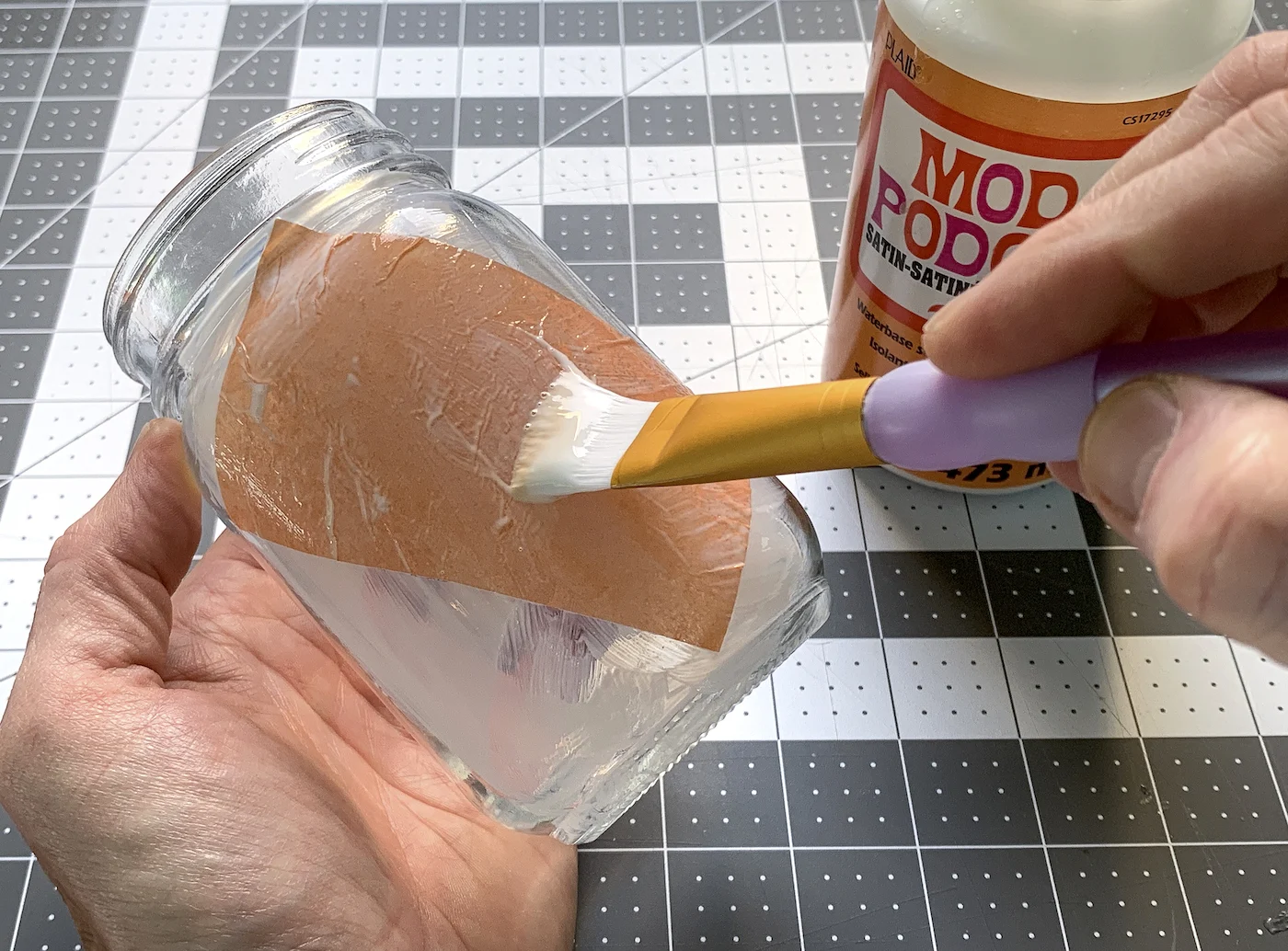 Painting Mod Podge on top of a piece of orange tissue paper with a paintbrush