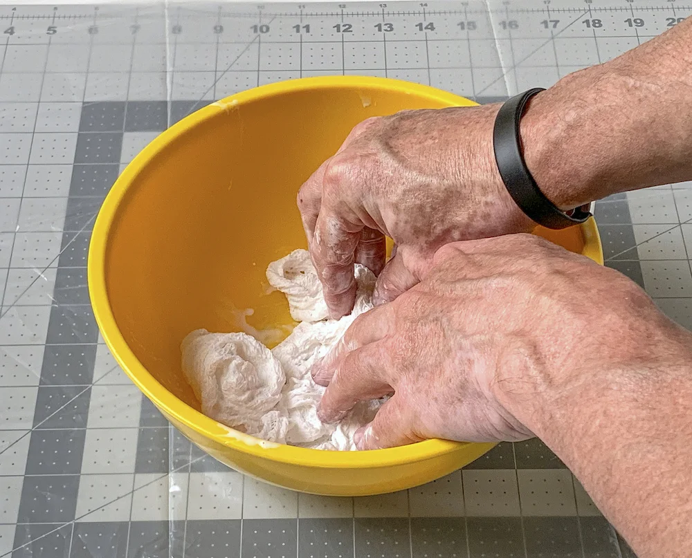 Two hands pressing cheesecloth into the fabric stiffener in a bowl