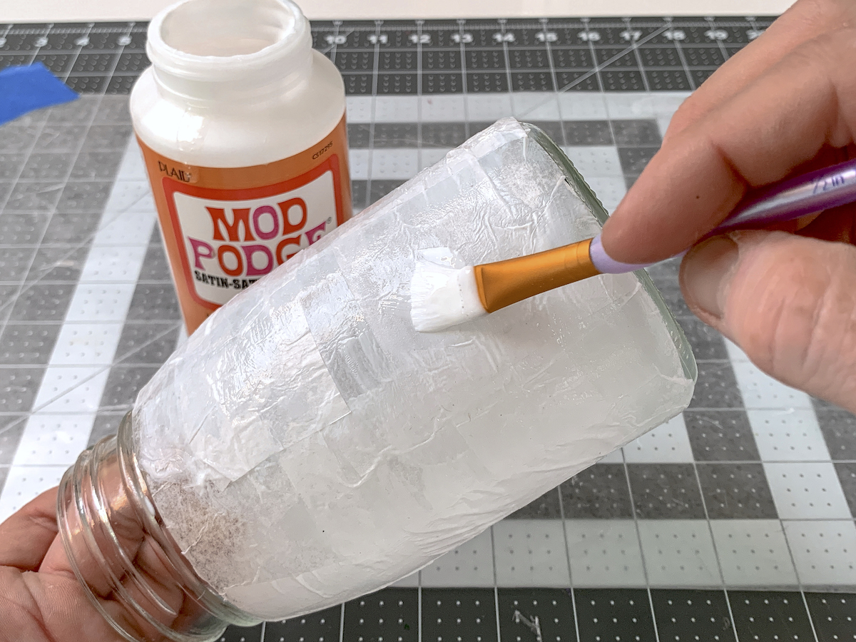 Brushing a layer of Mod Podge over tissue paper on a mason jar