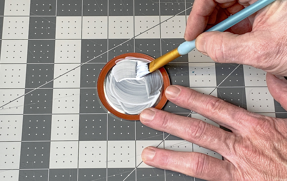 Painting Mod Podge onto the back of a mason jar lid with a paintbrush
