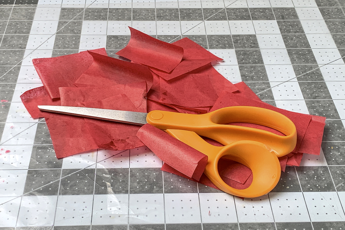 Papel de seda vermelho cortado em quadrados com uma tesoura em cima
