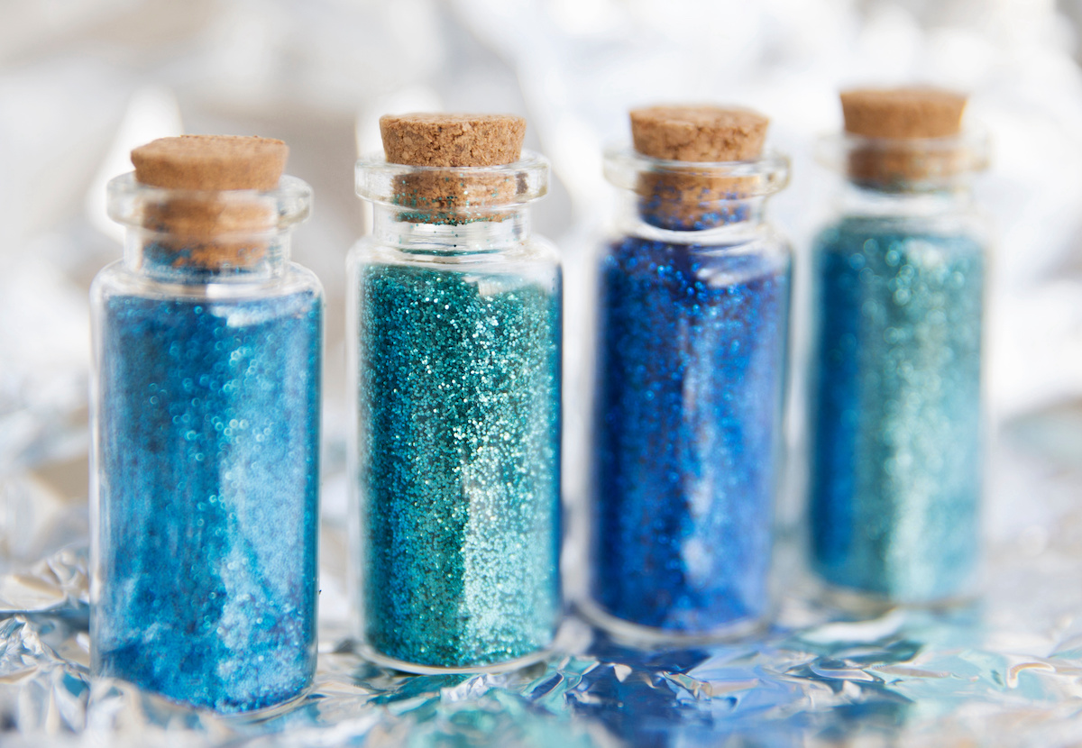 Bottles of blue glitter on a silver background isolated. Powder in transparent bottles