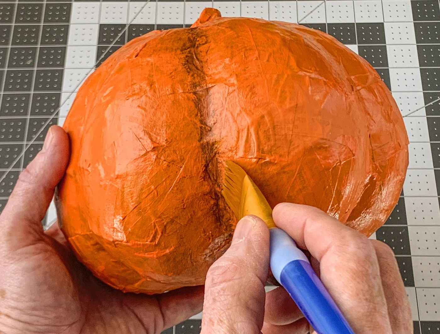 Adding brown paint between the pumpkin ribs with a paintbrush