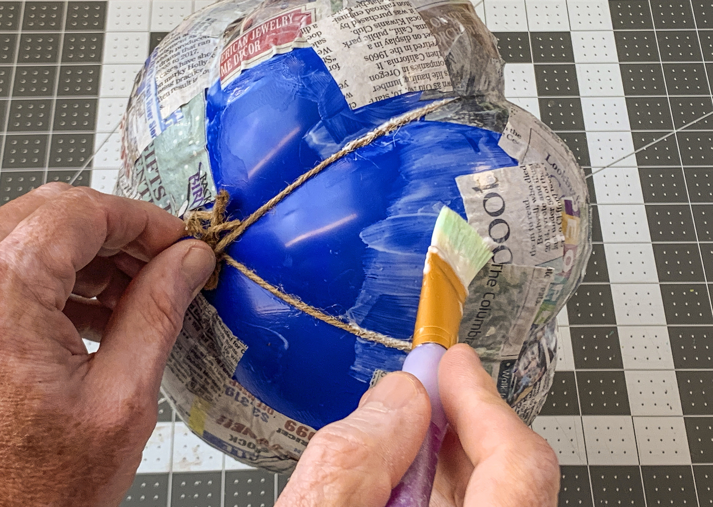 Covering the balloon and twine with decoupage medium and newspaper
