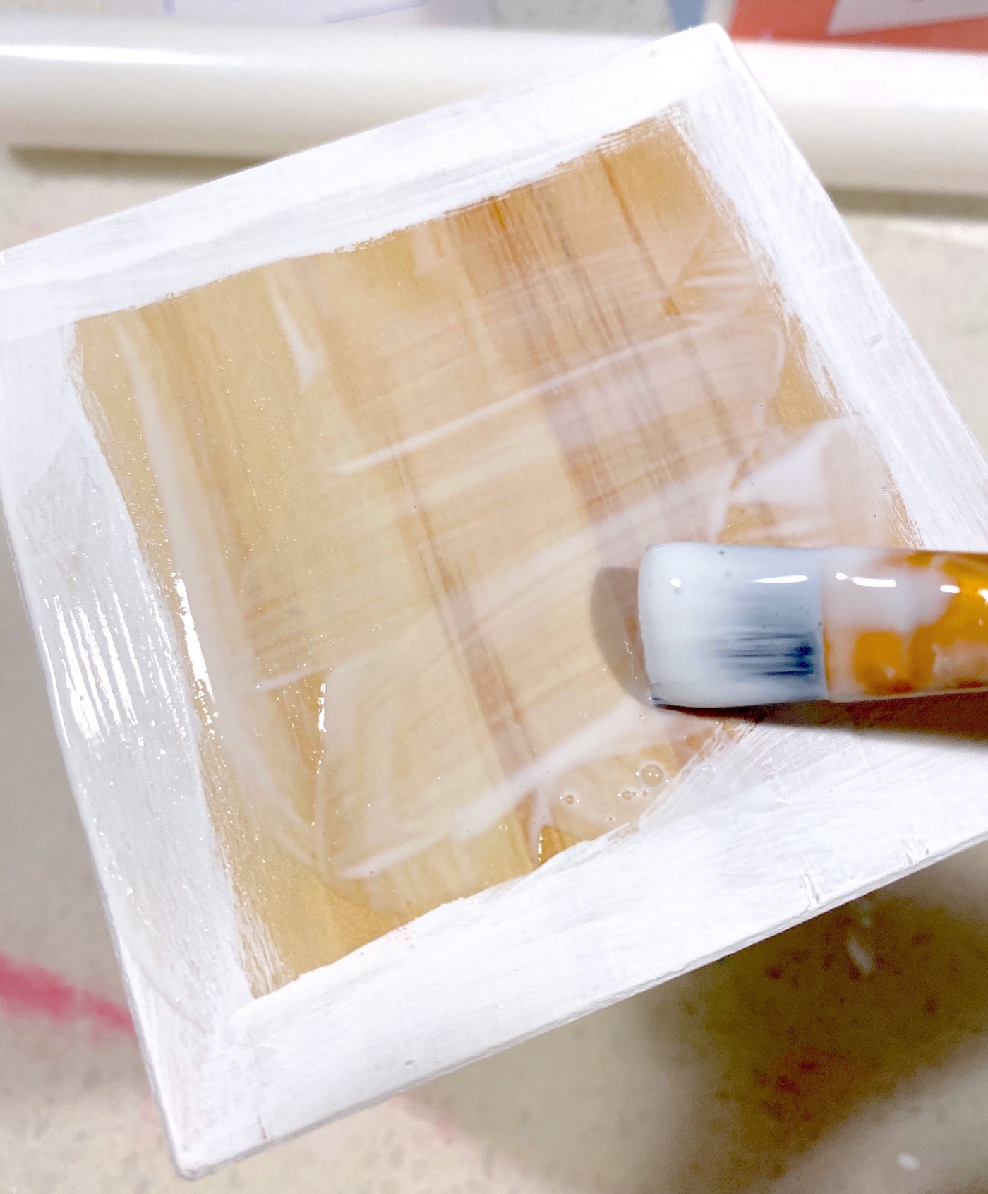 Applying decoupage medium to a side of a wood block with a paintbrush