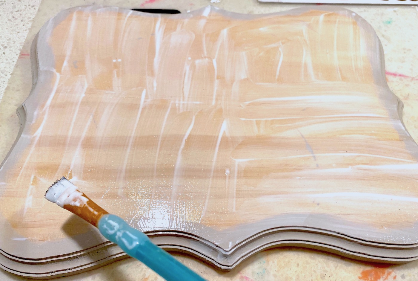 Applying Mod Podge to the top of the wood plaque with a brush