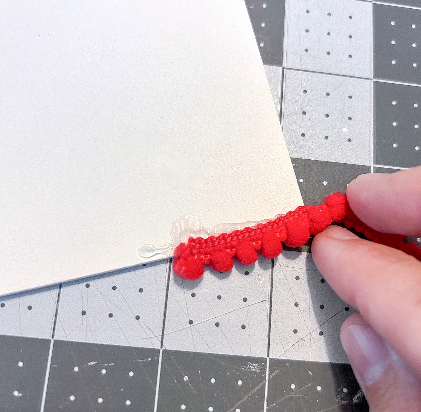 Gluing red pom pom trim around a wood door hanger painted white