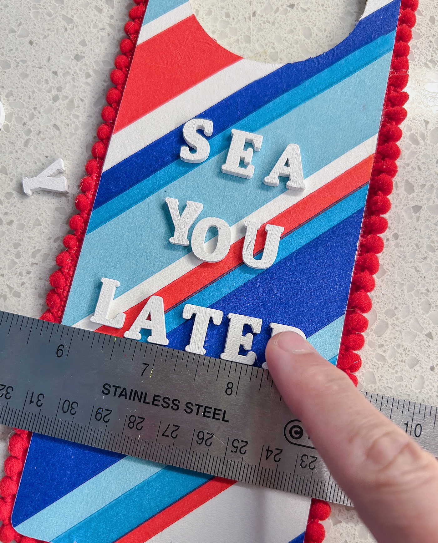 Using a ruler to line up wood letters and glue them to the surface of the door hanger