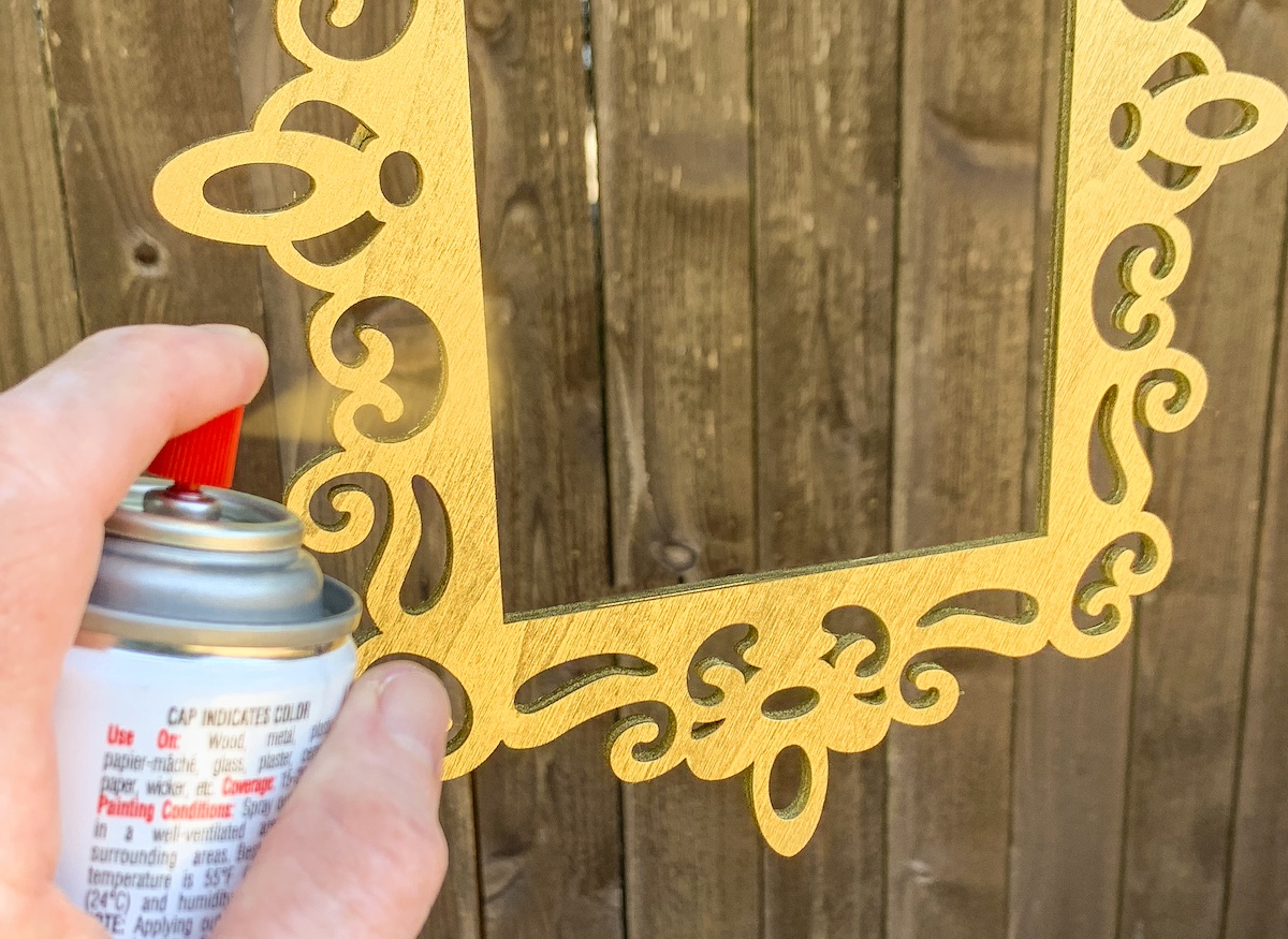 Spraying a wood lasercut frame with gold spray paint