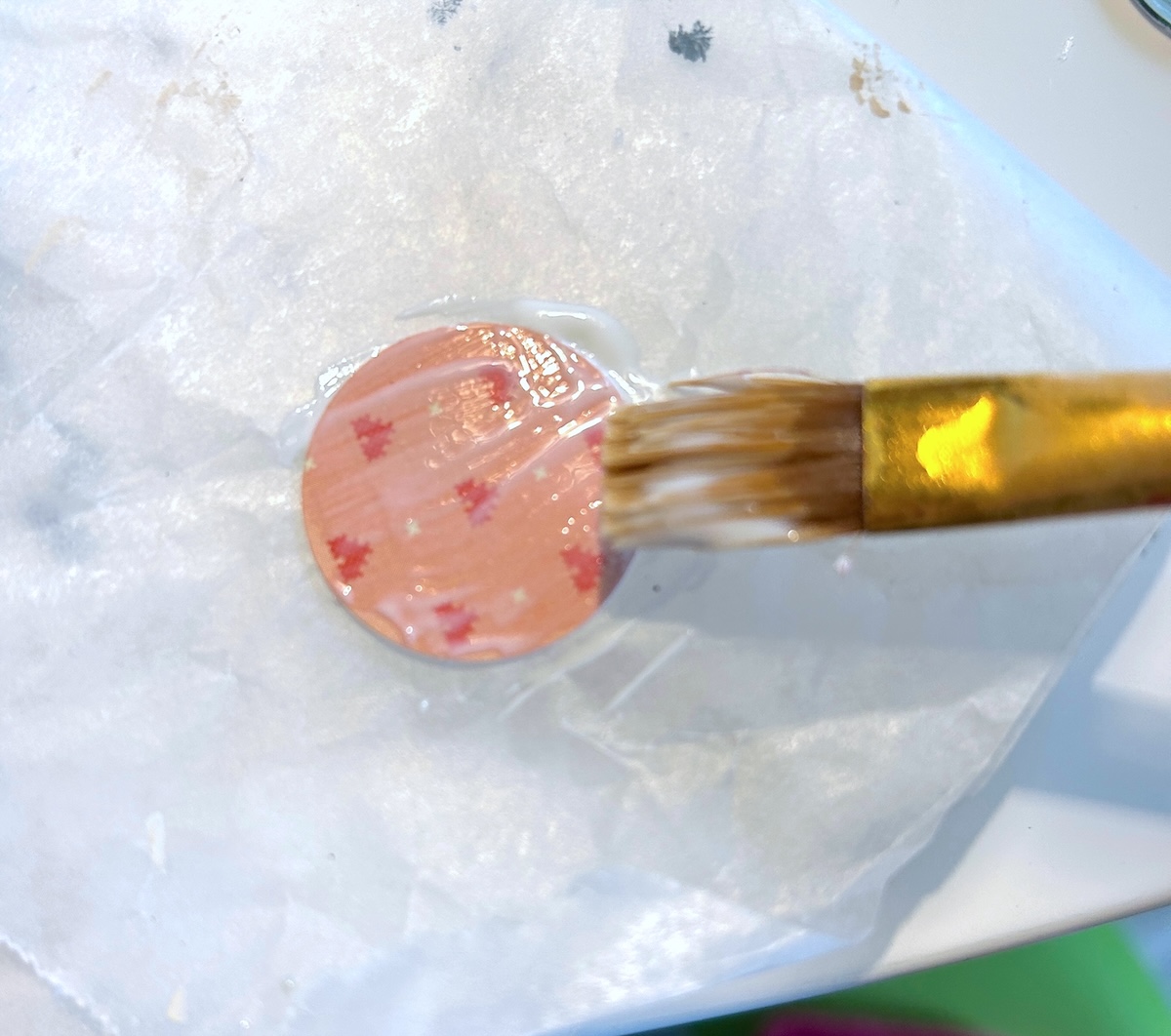 painting mod podge onto a paper circle with a brush