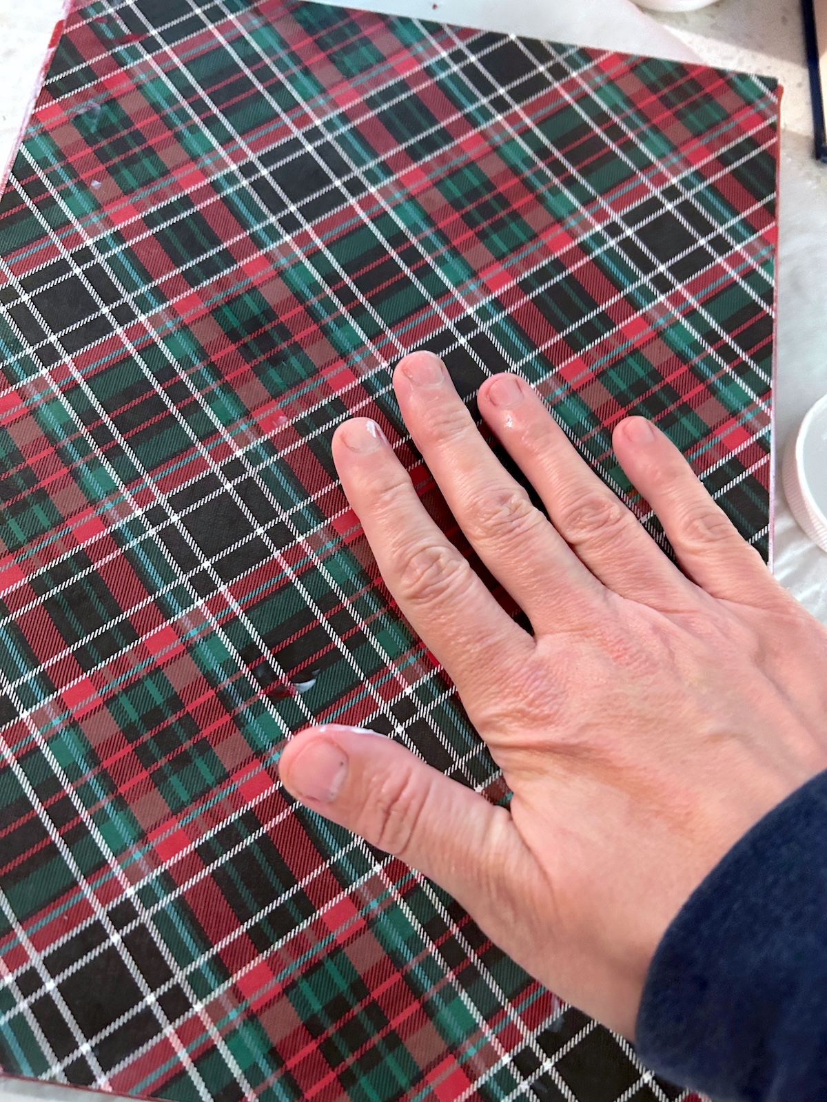smoothing plaid paper down onto the canvas